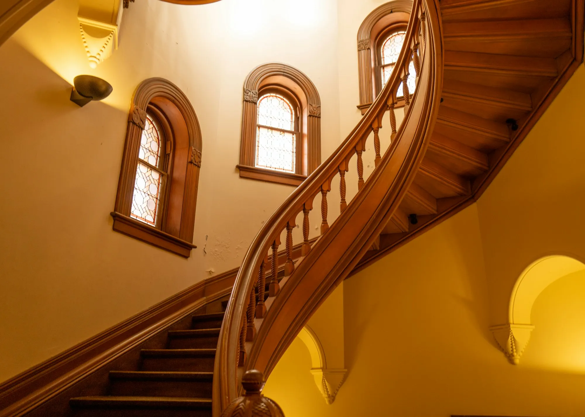 Warm curved timber staircase with arched windows